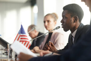 Side view of African businessman performing during conference he sitting at the table and speaking into the microphone