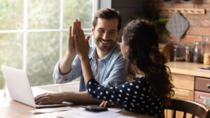 Happy man and woman at kitchen table with laptop giving each other a high five