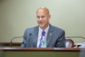 Senator Pat Stefano sits at a table and speaks into a microphone at a public meeting.