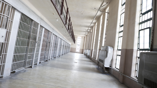 Two levels of prison cells on the left facing prison windows on the right, with white floor hallway in between.