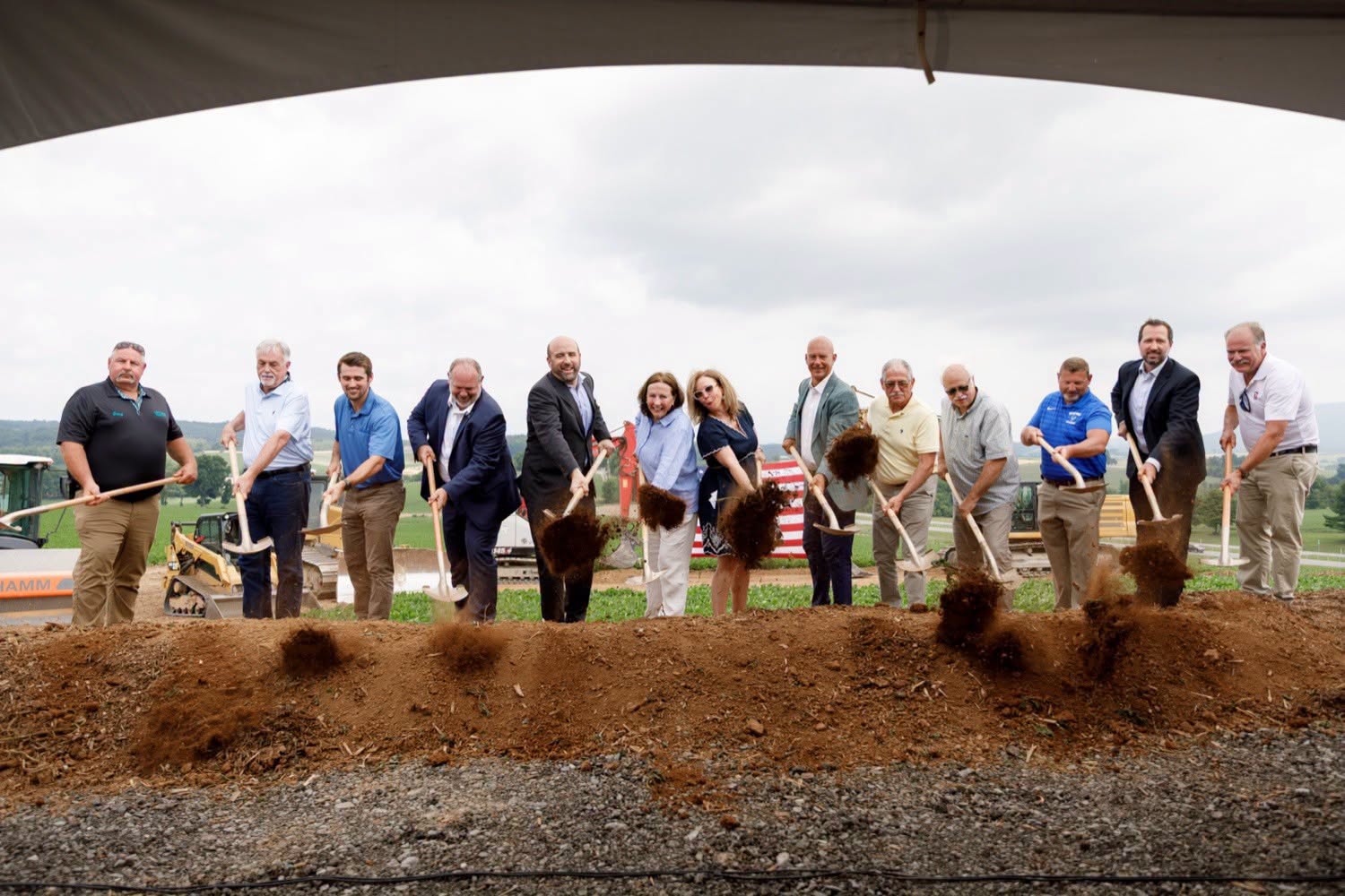 Community leaders and local officials participate in a ceremonial groundbreaking for the Bette Brown Slayton Business Park, standing in a line with shovels as they toss dirt during the event.